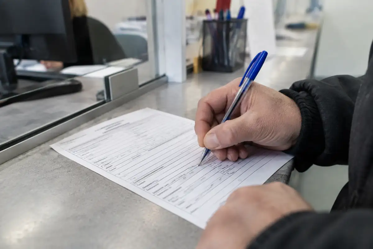 Main remplissant un formulaire de plainte au comptoir d'un guichet