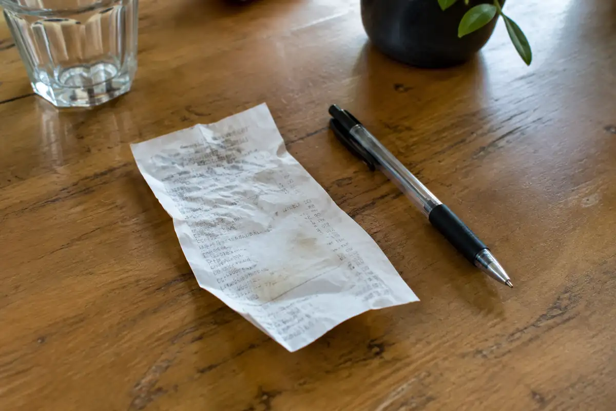 Reçu de restaurant froissé posé à côté d'un stylo sur une table